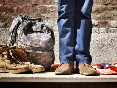 Man in civilian clothes standing next to military backpack by Benjamin Faust